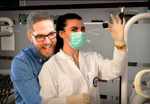dnatured-harassmentsmall A man is hugging a female scientist from behind as she holds a sample, she looks at him, annoyed.